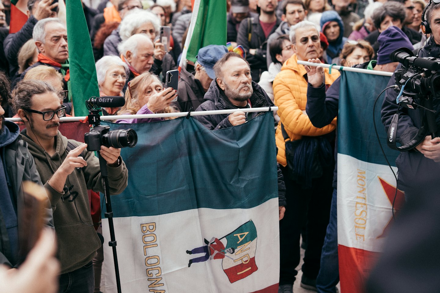Due uomini filmano una folla con striscioni di protesta durante un evento.