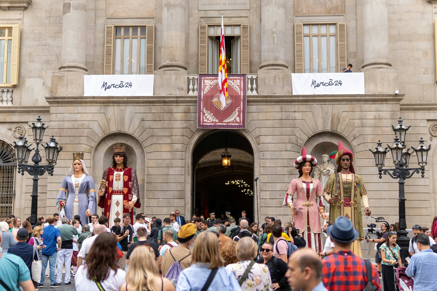 Persone riunite con figure giganti per una festa culturale in una piazza storica.
